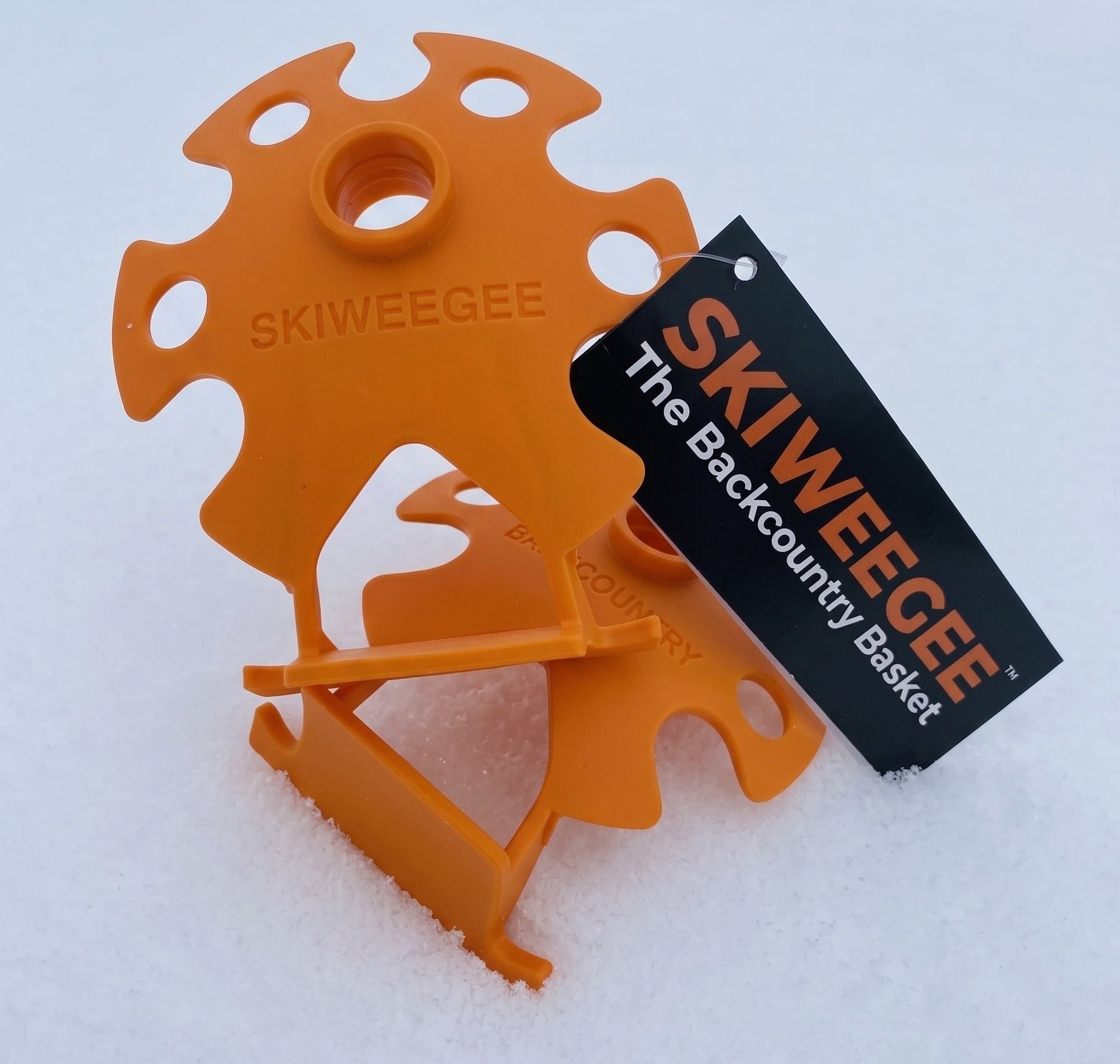 Two orange ski baskets in snow with a Skiweegee tag reading "The Backcountry Basket"