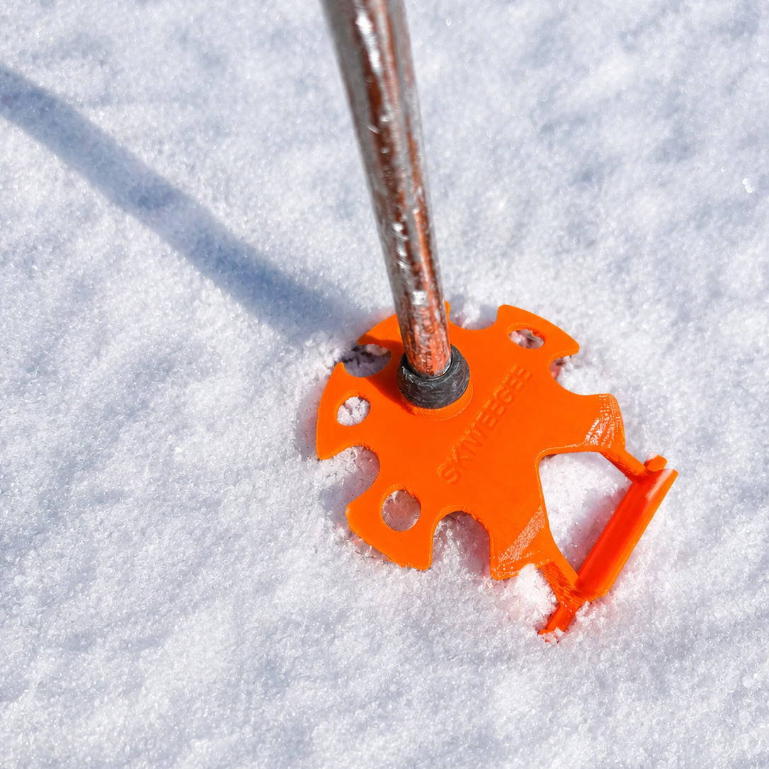 Close-up of an Orange Skiweegee basket fitted on a ski pole tip, pressed into snow